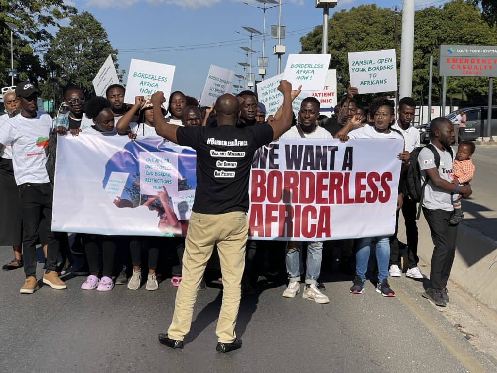 Crowd of protesters holding signs and a large banner reading 'We want a borderless Africa' during a street march.