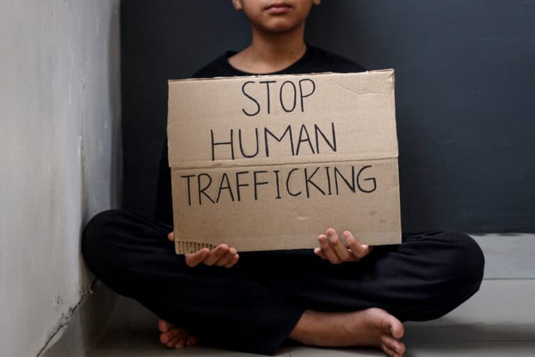 Person sitting cross-legged holding a cardboard sign that reads 'STOP HUMAN TRAFFICKING'.