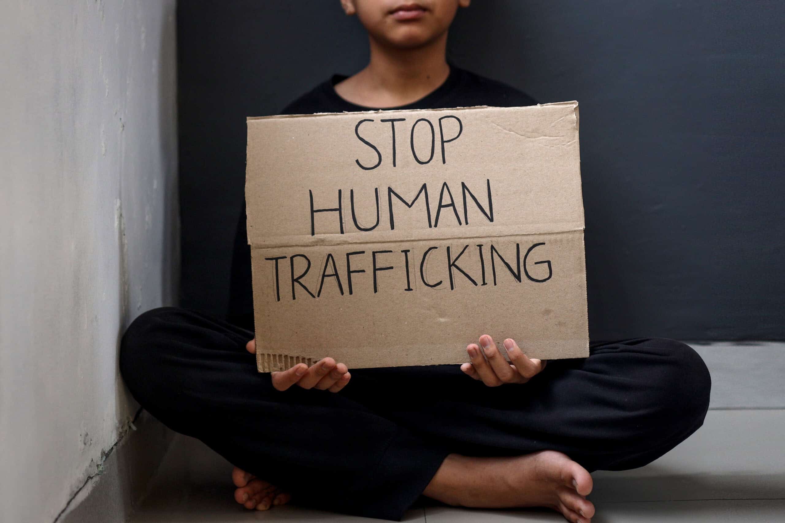 teen-holds-stop-human-trafficking-sign-2026-03-24-03-36-01-utc - Africans Rising - Africans Rising Person sitting cross-legged holding a cardboard sign that reads 'STOP HUMAN TRAFFICKING'.