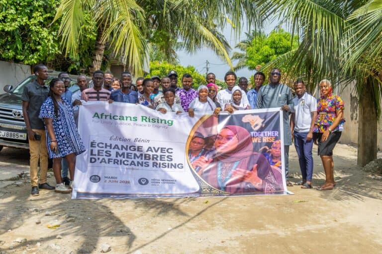 Group of people posing outdoors under palm trees, holding a banner for Africans Rising.