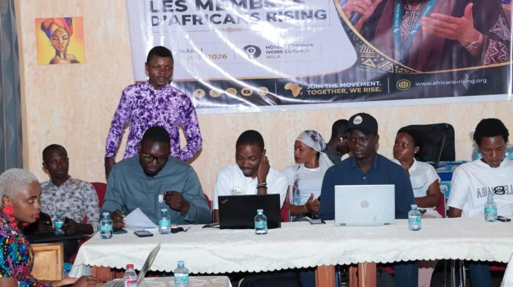 Panel of seven people seated at a long table with laptops and water bottles during a discussion, banner for Africans Rising in the background.