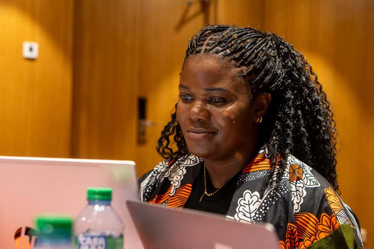 Woman with braided hair looking at a laptop in a wood-paneled room, focused on the screen.