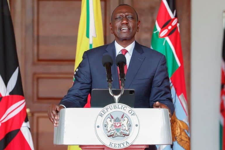 Male Kenyan official speaking at a podium with the Republic of Kenya seal, flags behind him.