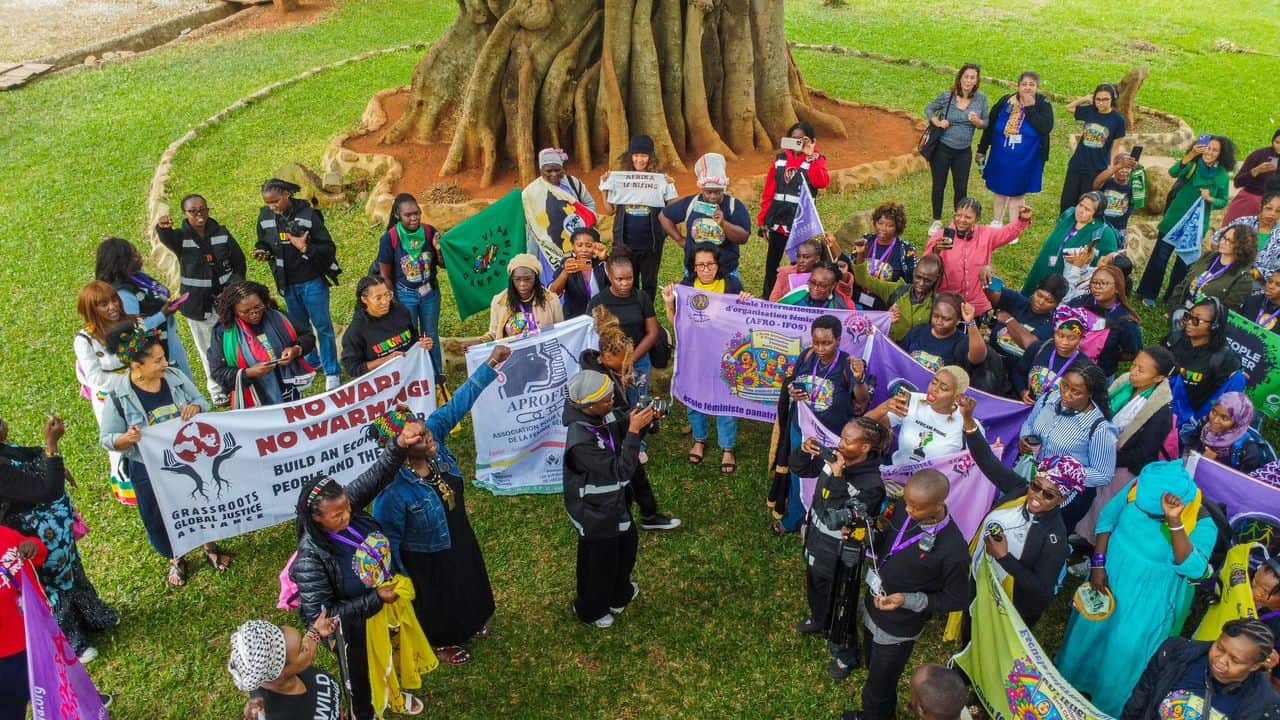 A diverse group of people in a circle holding banners for climate justice outdoors near a large tree, posing for a group photo during a rally.